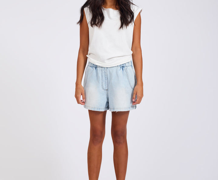 Person wearing a white sleeveless top and light blue denim shorts on a plain background