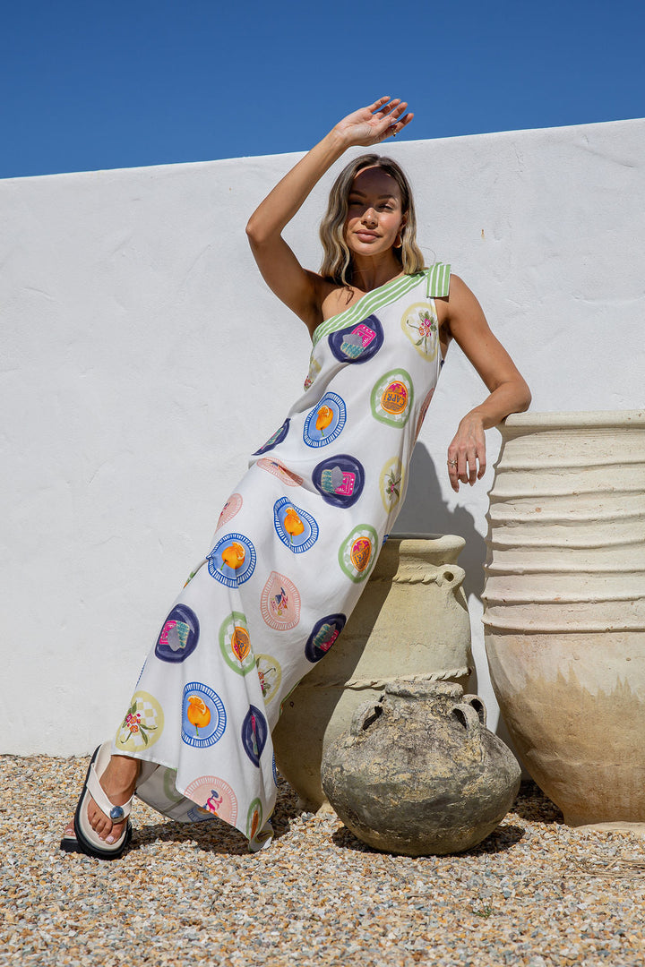 Woman wearing a colorful dress with abstract patterns against a white wall and blue sky.
