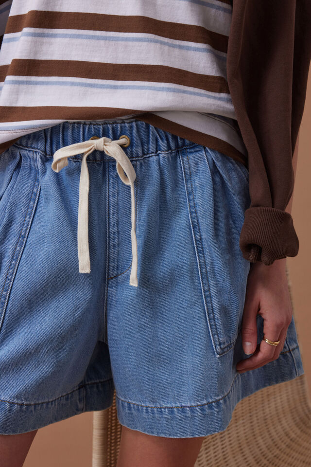 Person wearing blue denim shorts with a drawstring, standing against a beige background.