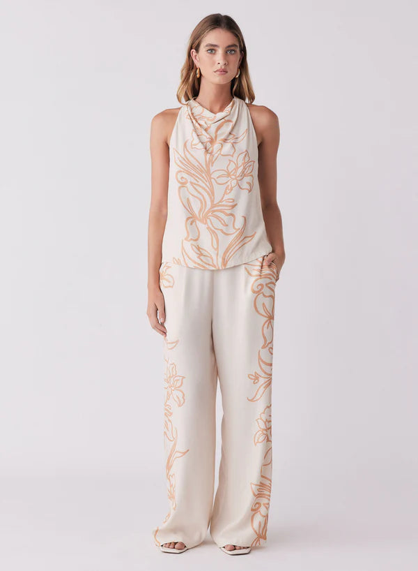 Woman wearing a sleeveless top and wide-leg pants with floral patterns on a white background