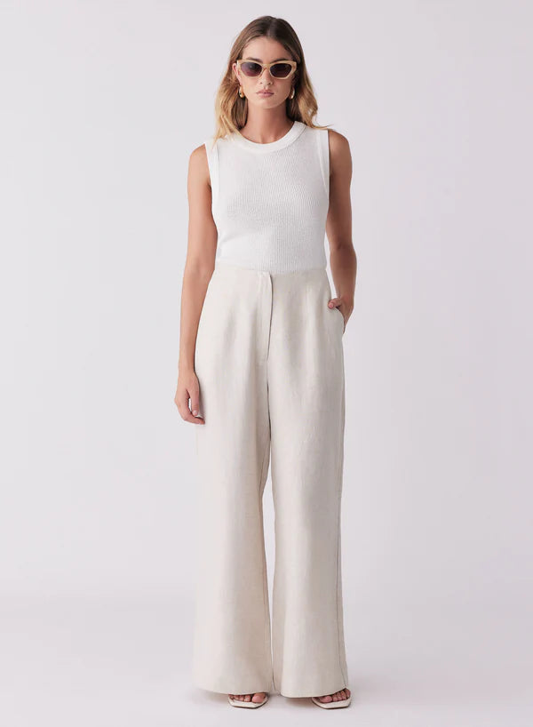 Woman wearing a white sleeveless top and beige wide-leg pants on a white background
