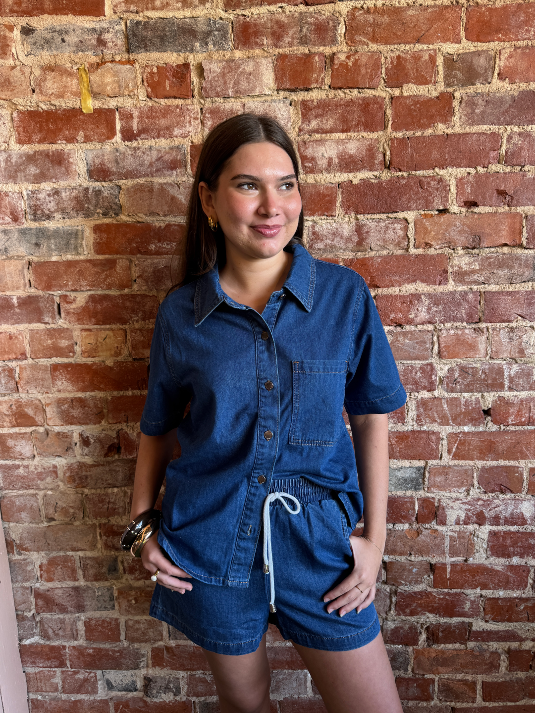 Woman wearing a blue denim outfit standing against a brick wall.