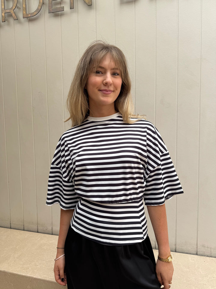 Woman wearing a black and white striped shirt against a neutral wall.