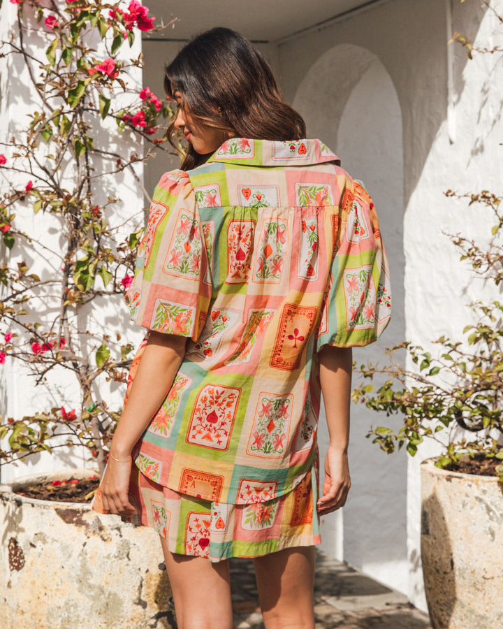 Woman wearing a colorful patterned dress standing in front of a white wall with plants.
