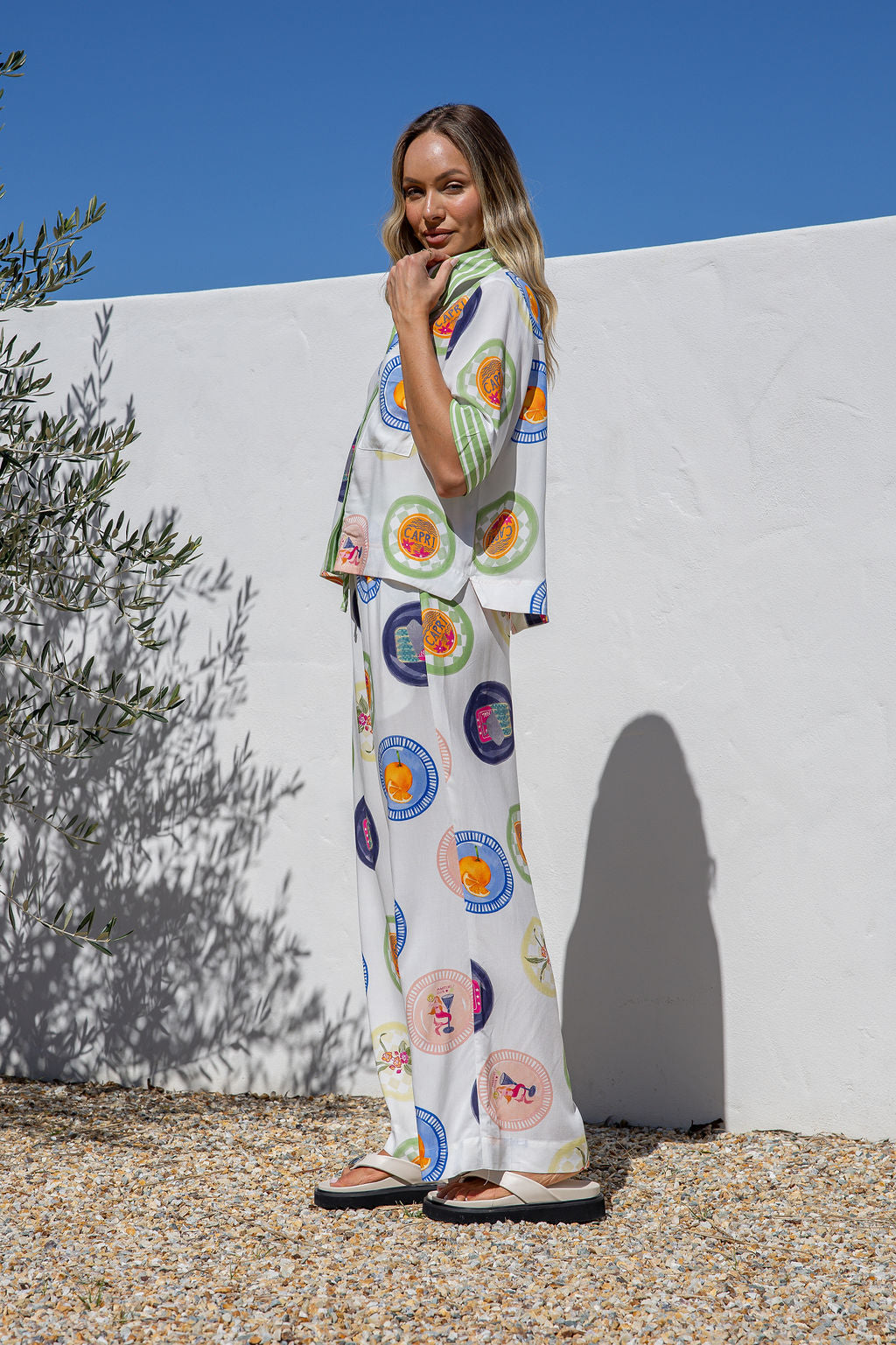 Woman wearing a colorful outfit standing against a white wall with a blue sky.