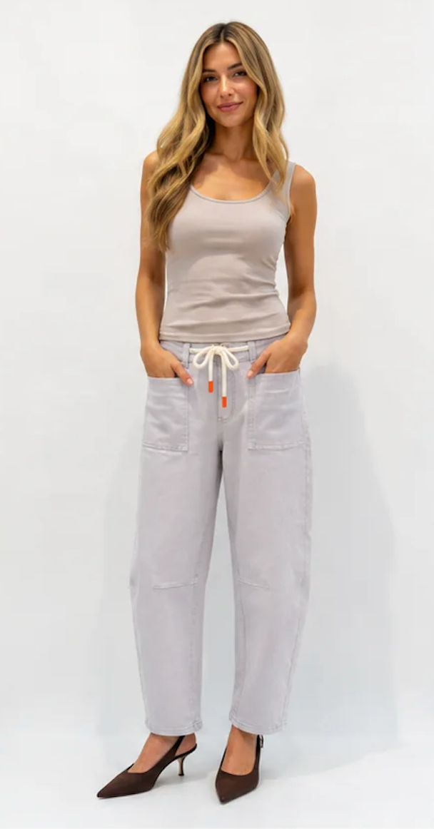 A woman modeling a light beige ribbed tank top and light gray drawstring pants with brown pointed-toe heels, standing against a plain white studio background.