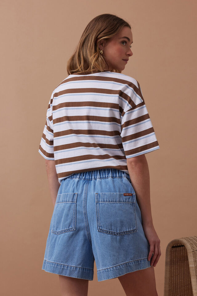 Woman wearing a striped shirt and denim shorts against a beige background