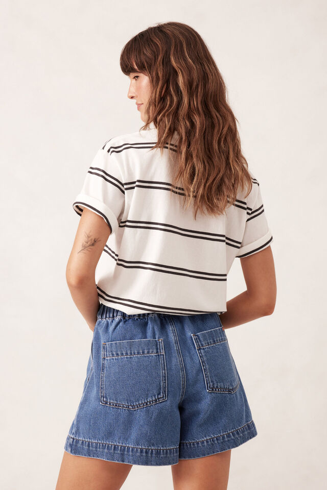 Woman wearing a striped shirt and denim shorts on a plain background