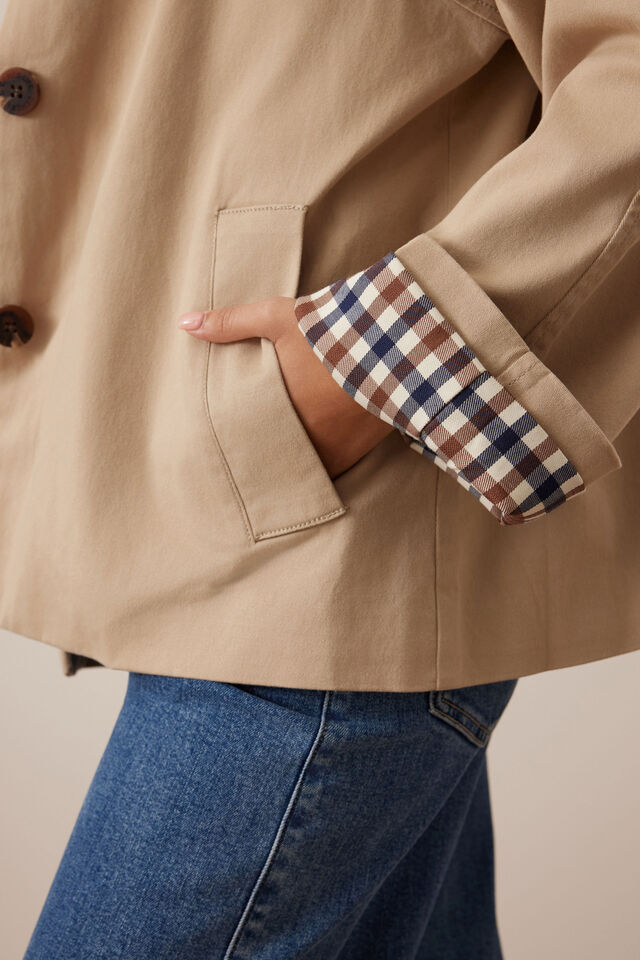 Close-up of a beige coat with plaid cuffs and blue jeans on a neutral background ceres life