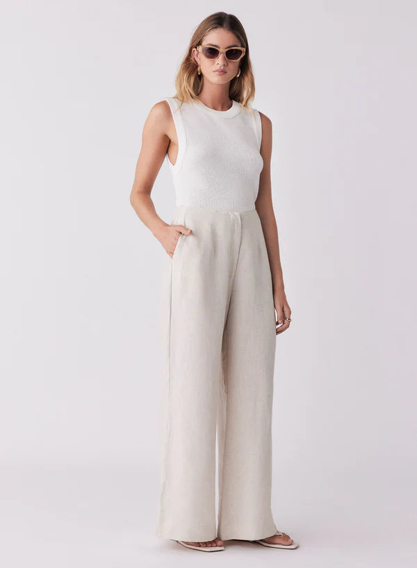Woman wearing a white sleeveless top and beige wide-leg pants on a white background