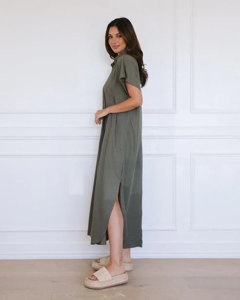 Woman wearing a green dress standing against a white paneled wall.