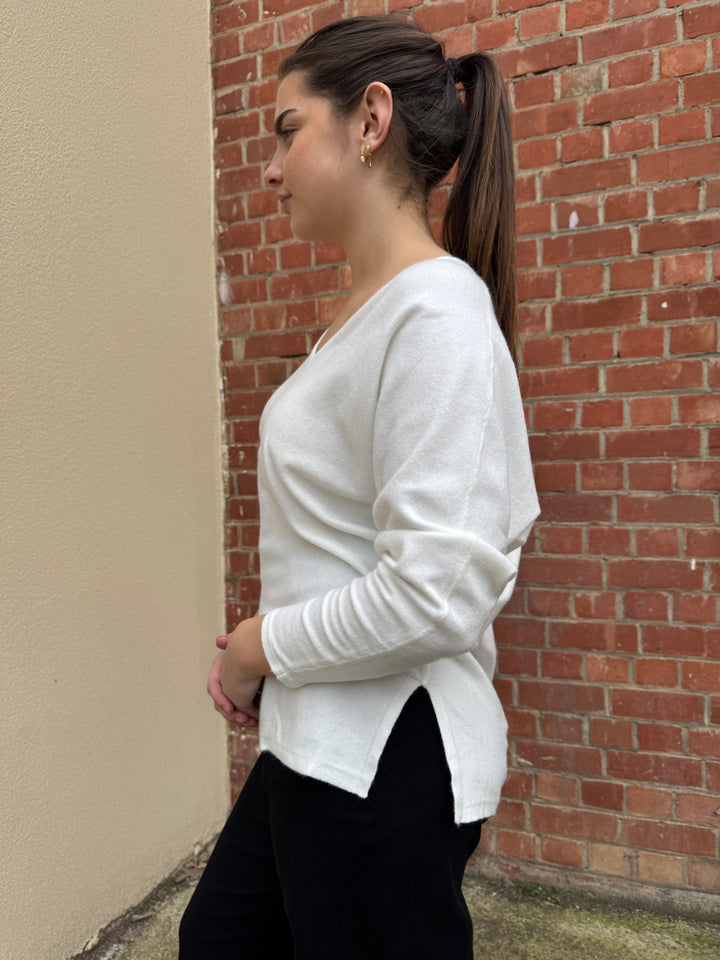 Person wearing a white long-sleeve shirt and black pants against a brick wall.