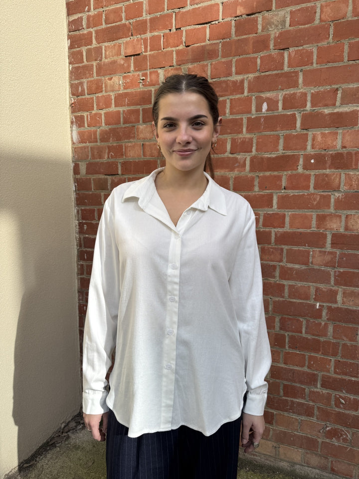 Stella wearing a white sunny girl shirt standing against a brick wall.
