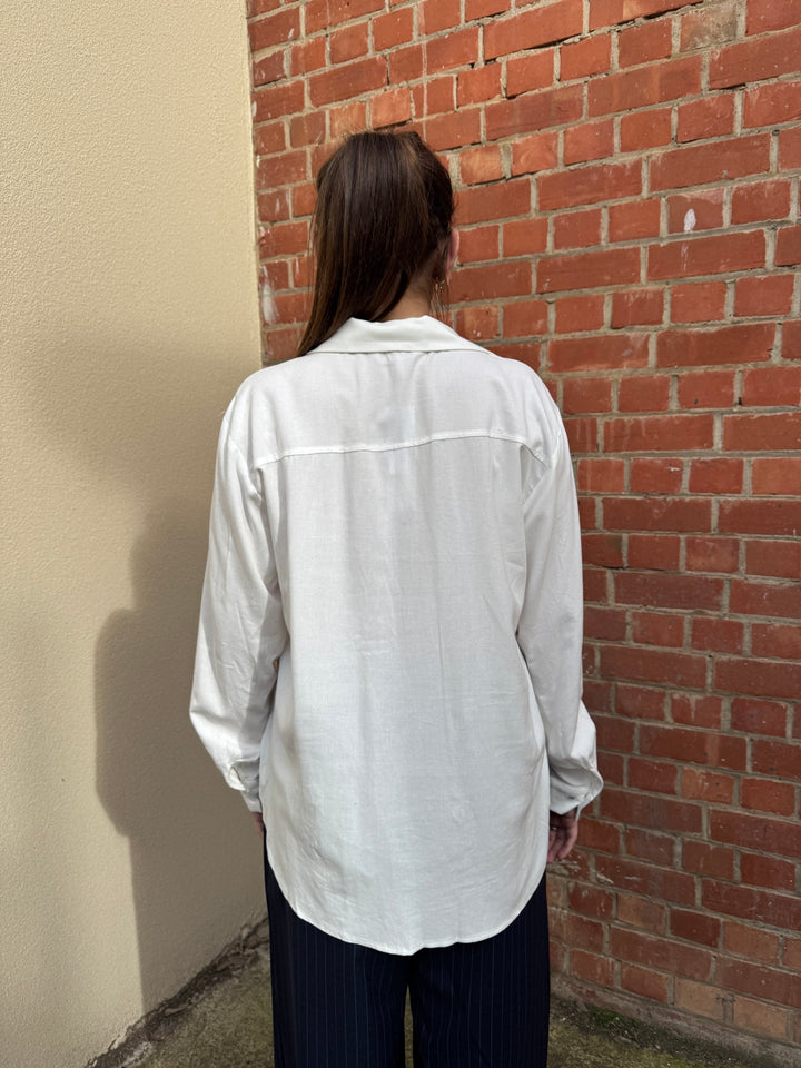 Person wearing a white shirt against a brick wall.