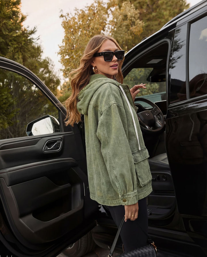 A woman wearing the smaibulun khaki hooded jacket and black sunglasses stands next to an open black vehicle door, holding a black quilted handbag.