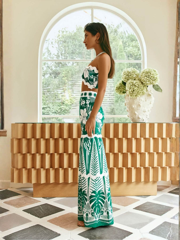 Woman in a green and white patterned set by Smaibulun standing in a room with a wooden console table and floral arrangement.