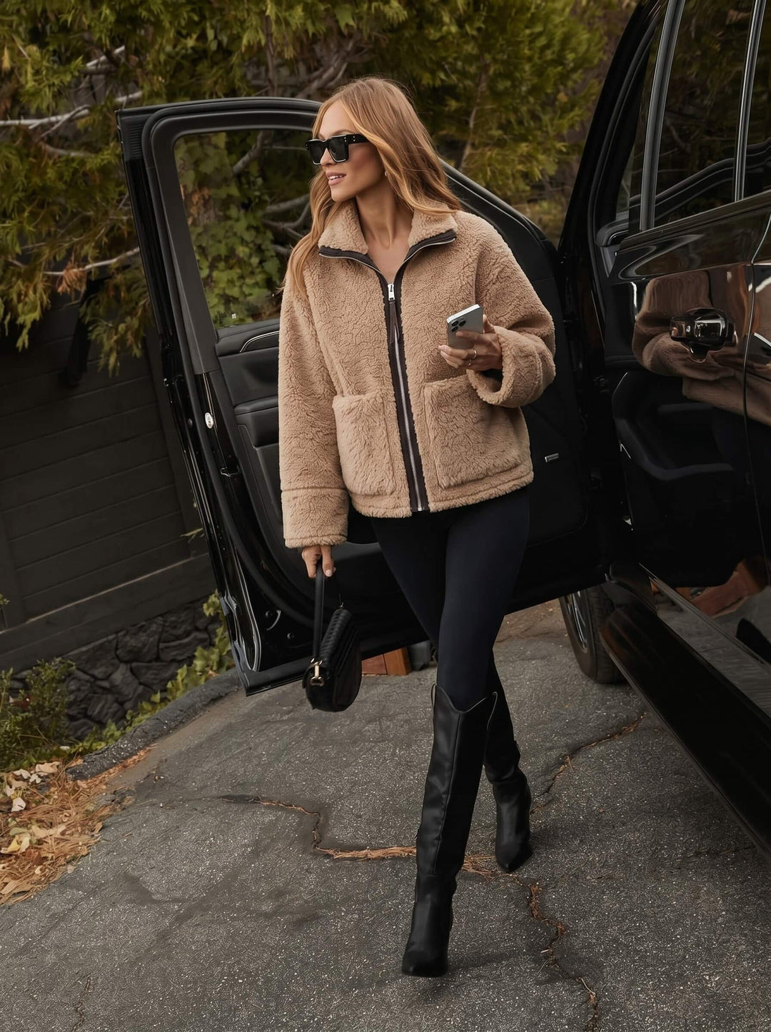 Woman in a beige smaibulun jacket and black boots getting out of a car.