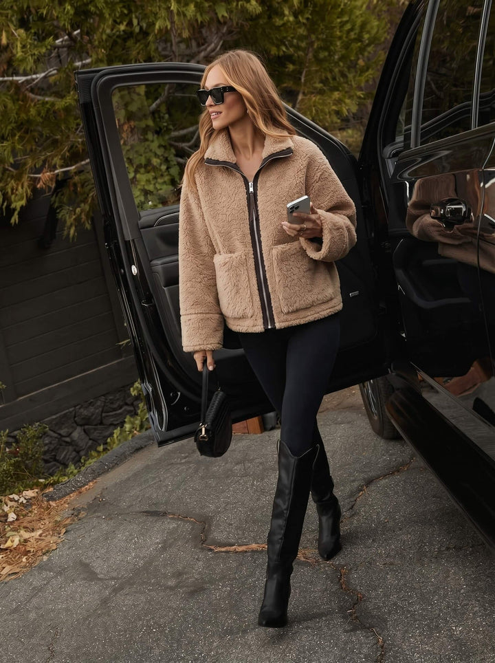 Woman in a beige smaibulun jacket and black boots getting out of a car.