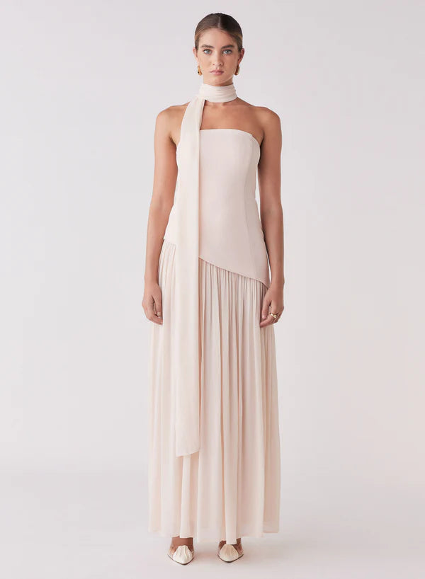 Woman wearing a long, flowing beige dress with a white background