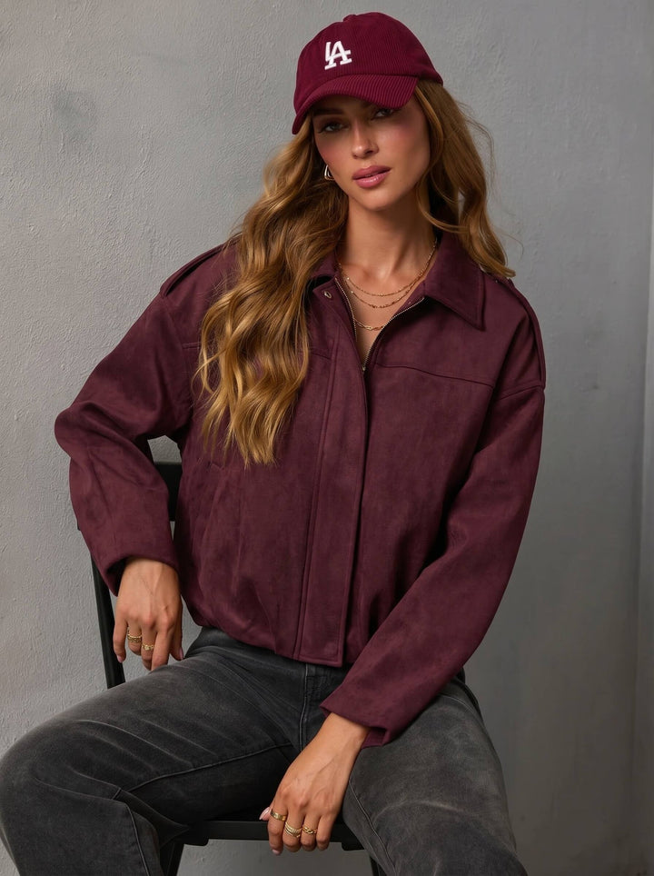 Woman wearing the yuzu bomber from smaibulun jacket and cap sitting against a gray background