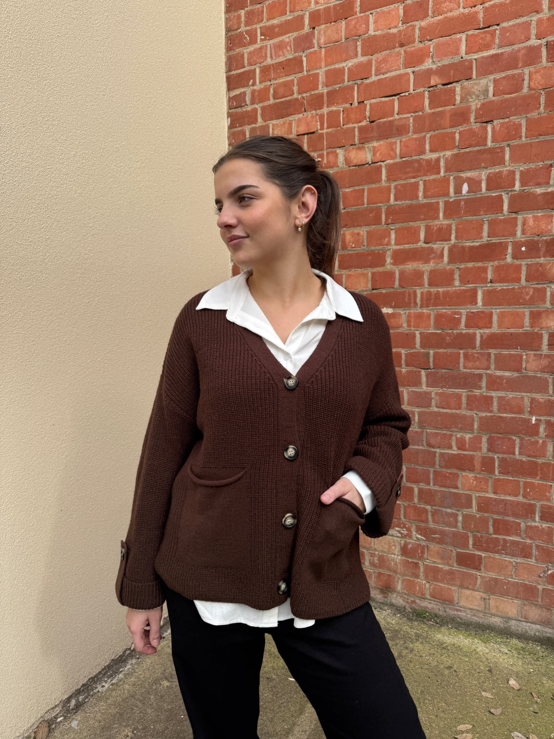 Person wearing a brown sunny girl coat and white shirt against a brick wall.