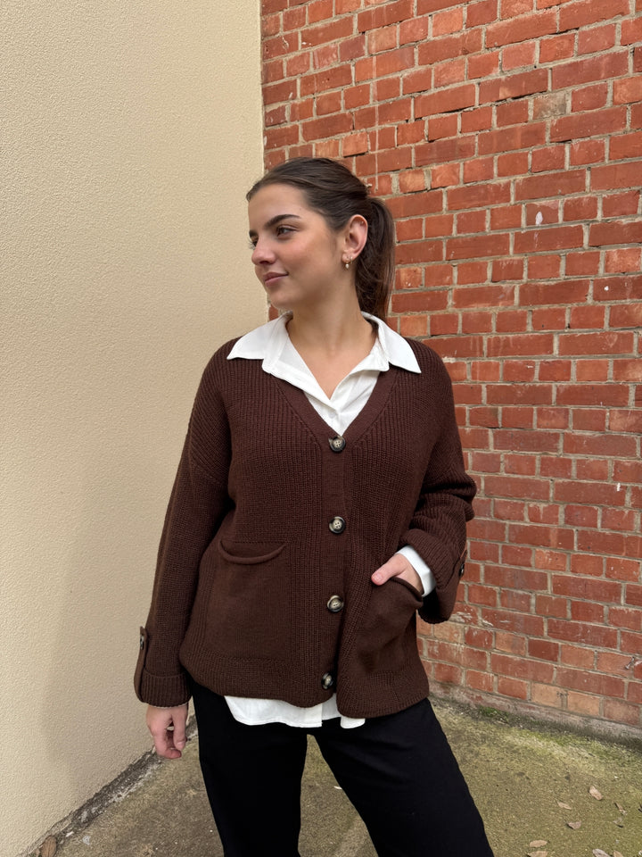 Person wearing a brown sunny girl coat and white shirt against a brick wall.